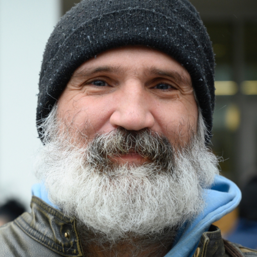 older man with white beard wearing black hat softly smiling